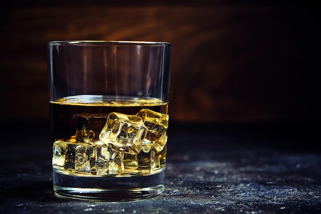 Glas gekühlter Whisky mit Eiswürfeln auf Holzhintergrund im Keller.