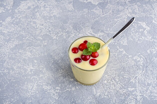 Glas gelber Mango- oder Bananenjoghurt oder Smoothie auf grauem Hintergrund serviert mit Beeren und Minze. Gesundes Milchgetränk