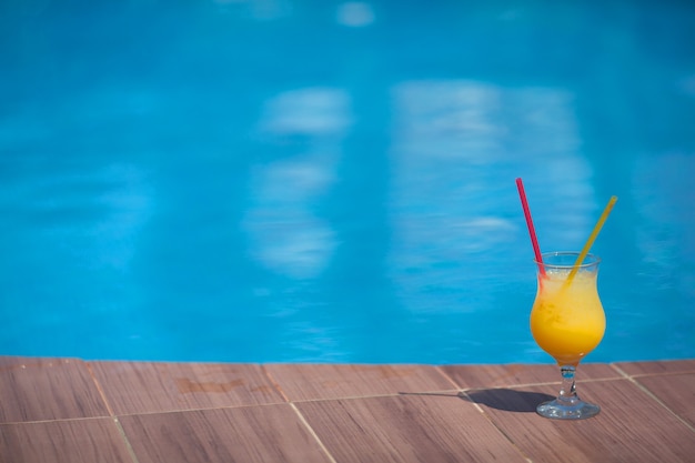 Glas gelber Saft mit Eis gegen die Wand des Pools im Sommer