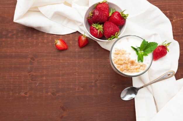 Glas gesunder Erdbeerjoghurt mit frischen Beeren auf Holztisch