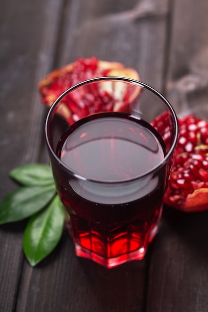 Glas Granatapfelsaft mit Stücken und Blättern von Granatapfelfrüchten auf einem dunklen Holztisch