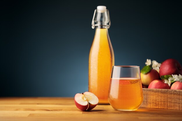 Glas hausgemachten Apfelwein oder Saft, rote frische Äpfel aus dem Garten und eine Flasche auf Hintergrund
