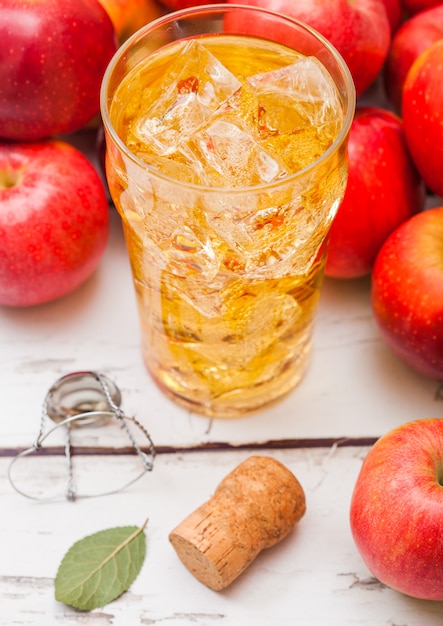 Glas hausgemachten Bio-Apfelwein mit frischen Äpfeln auf Holztisch, Glas mit Eiswürfeln