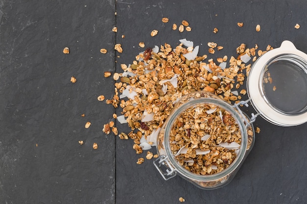 Glas hausgemachtes Bio-Müsli mit Kokos und Pekannüssen auf schwarzem Hintergrund lecker