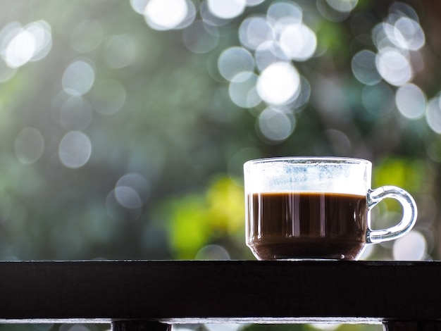 Glas Kaffee auf Holztisch über grünem abstraktem Hintergrund