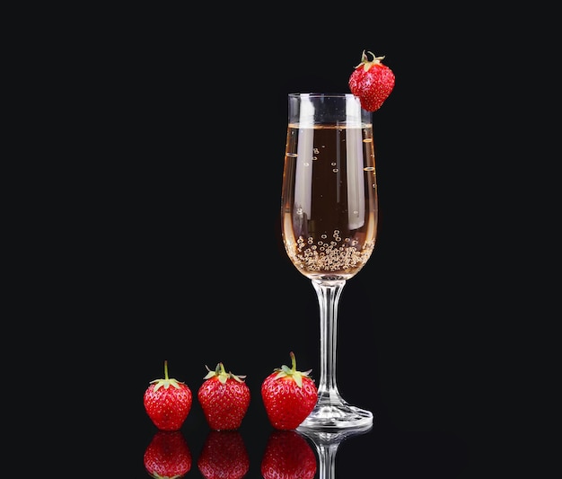 Glas kalter Champagner mit Erdbeeren auf schwarzem Hintergrund