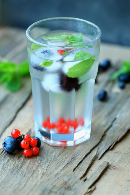 Glas kaltes erfrischendes Sommergetränk mit Beeren und Eiswürfeln auf dem Tisch aus nächster Nähe