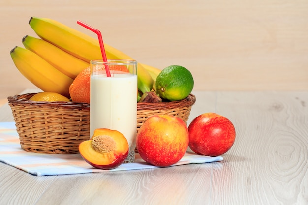 Glas köstlicher Joghurt mit Minze und frischen Erdbeeren, Banane, Limette, Nektarine in einem Weidenkorb auf einem Holztisch