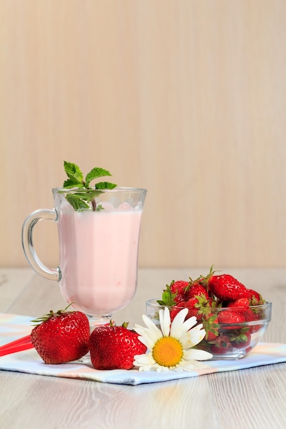 Glas köstlicher Joghurt mit Minze und frischen Erdbeeren, Kamille auf einem Holztisch mit Serviette