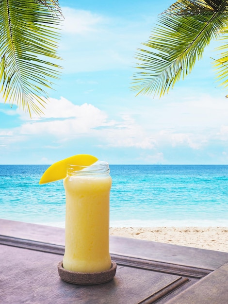 Glas Mangosaft über Strand und blauem Himmelshintergrund