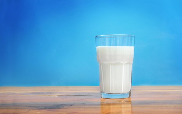 Glas Milch auf Holzoberfläche vor blauem Hintergrund