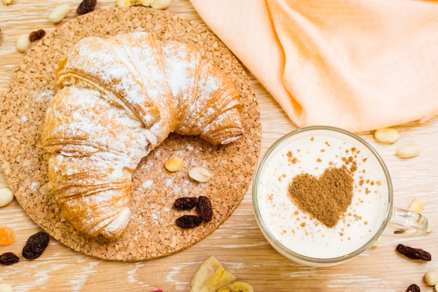 Glas Milch mit Herzen vom Zimt und vom Hörnchen im Puderzucker auf einem Holztisch