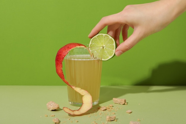 Glas mit Apfelcider und einer Limette in weiblicher Hand auf grünem Hintergrund