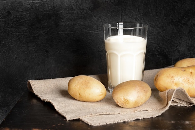 Foto glas mit bio-getränk aus kartoffeln und kartoffelknollen auf schwarzem hintergrund selektiver fokus