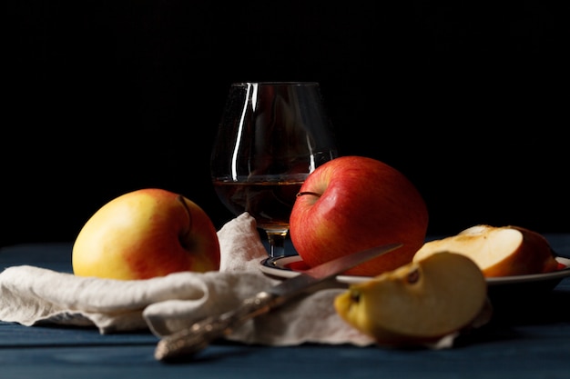 Glas mit Calvados Brandy und gelben Äpfeln auf einem Holztisch