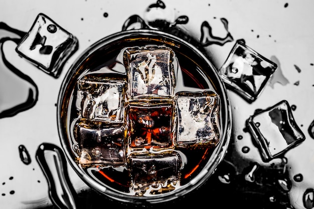 Glas mit Cola und Eiswürfeln, umgeben von Eiswürfeln und Wassertropfen