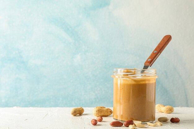 Glas mit cremiger Erdnussbutter und Löffel und Erdnuss auf weißem Tisch