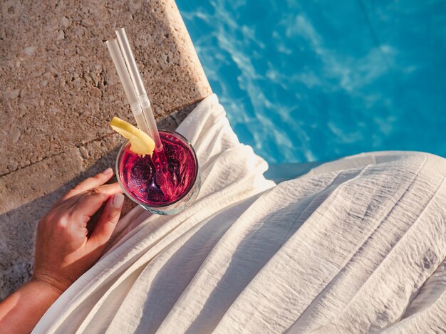 Glas mit einem Cocktail von Person neben einem Pool gehalten