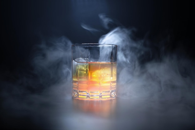 Glas mit Eisorangengetränk auf schwarzem Hintergrund mit Rauch