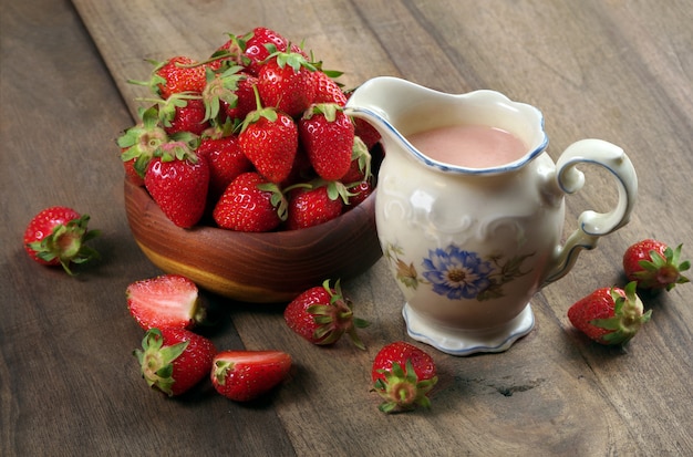 Glas mit Erdbeermilch, reife Erdbeeren in einer Holzschale auf einem Holztisch