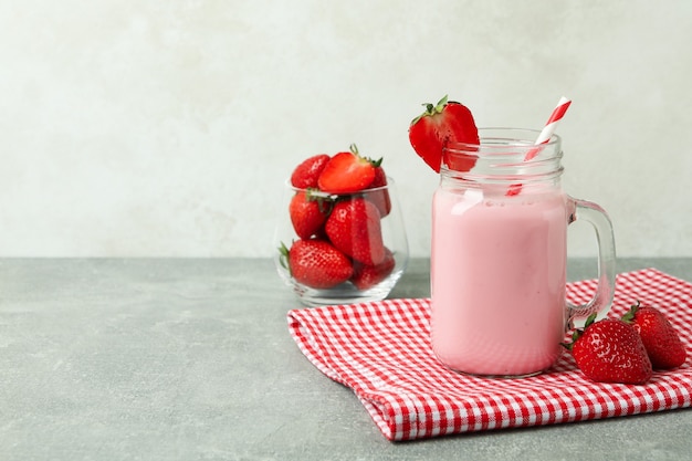 Glas mit Erdbeermilchshake und Zutaten auf grauem strukturiertem Tisch