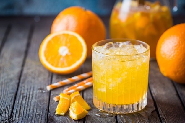 Glas mit frischem Orangensaft mit Eis und frischen Früchten auf dunklem Tisch