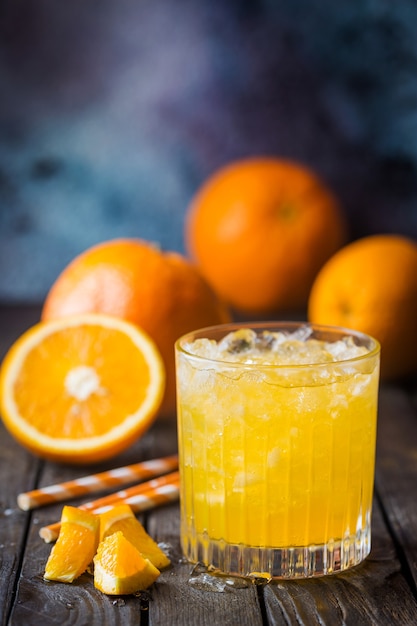 Glas mit frischem Orangensaft mit Eis und frischen Früchten auf dunklem Tisch