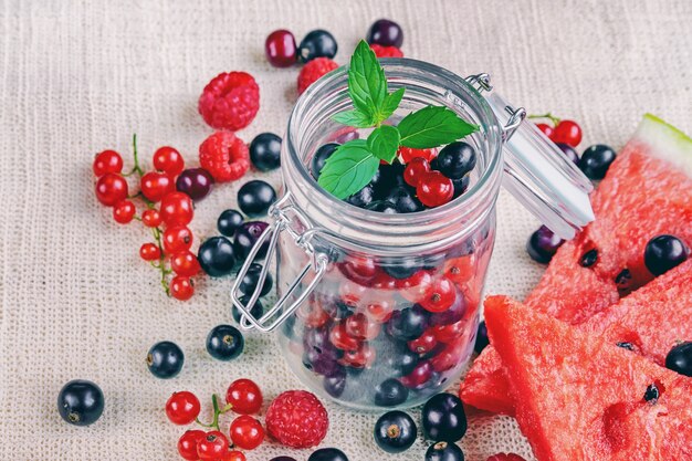 Glas mit frischen Johannisbeeren, Himbeeren, Wassermelonenscheiben und Minzblättern auf Leinentextilien