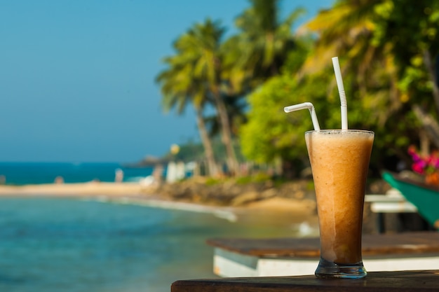 Glas mit Fruchtsaft frisch über dem Meer und Palmen