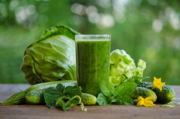 Glas mit grünem Smoothie auf einem Holztisch und Gemüse mit Minzblättern