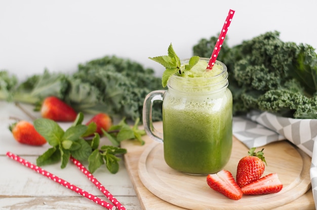 Glas mit grünem Smoothie mit Grünkohlblättern, Minze und Erdbeere