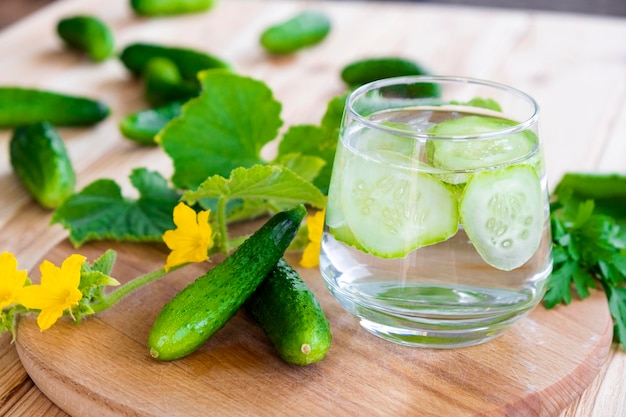 Glas mit Gurkenwasser auf Holzbrett mit frischen Gurken herum Hausgemachte Limonade aus frischen Gurken für sommerliche Erfrischungsdiät und Entgiftung