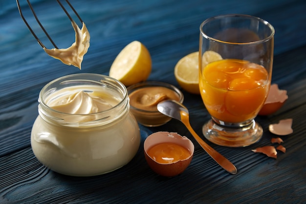 Glas mit hausgemachter Mayonnaise und Zutaten auf einem blauen Holztisch.