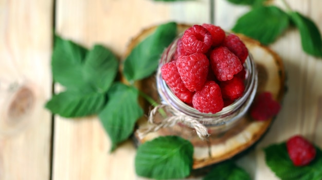 Glas mit Himbeeren und Himbeerblättern auf einer Holzoberfläche.