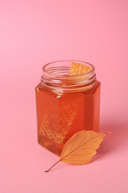 Glas mit Honig und Herbstblatt auf rosa Hintergrund