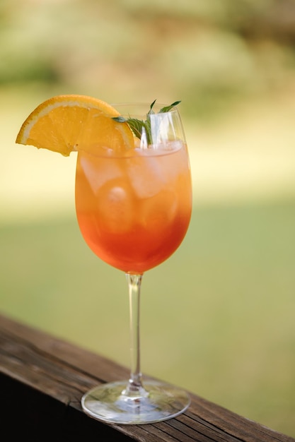 Glas mit orangefarbenem Alkoholgetränk Cocktail mit Orangenminzblatt und Eis auf Holzbrett