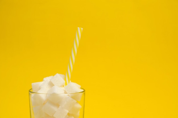Glas mit raffinierten Zuckerwürfeln und einem Trinkschlauch auf gelbem Hintergrund