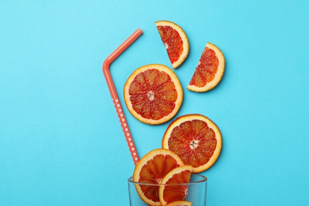 Glas mit roten Orangenscheiben und Stroh auf blauem isoliertem Hintergrund