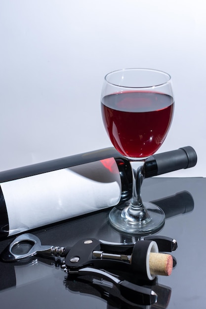 Glas mit Rotwein neben Flasche und Korkenzieher mit Korken