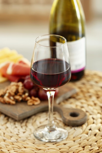 Glas mit Rotwein und leckeren Snacks auf einem Brett auf Weidenmatte