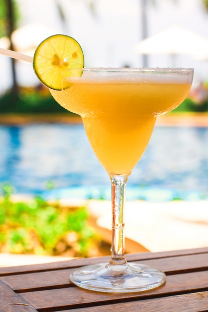 Glas mit süßem alkoholischem Cocktail auf Holztisch im exotischen Erholungsort