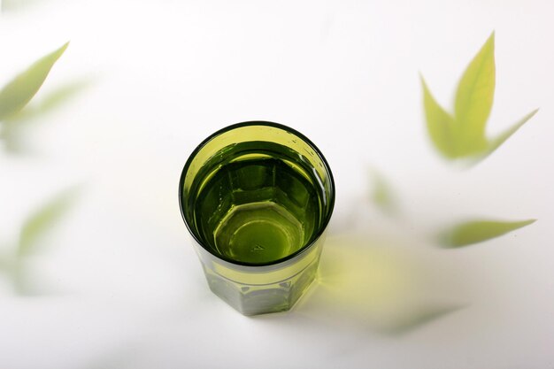 Glas mit Wasser und einem hellen Hintergrund mit Pflanzenblättern