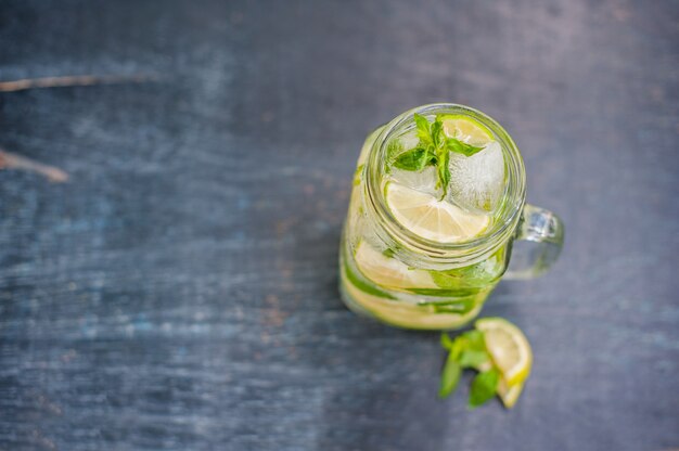 Glas Mojito mit Limetten- und Minzeiswürfel-Nahaufnahme auf dunkler Holzoberfläche