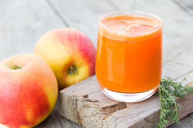 Glas orange Karottensaft mit Äpfeln auf Holz