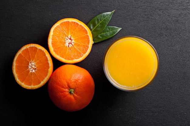 Glas organischer frischer Orange Smoothiesaft mit rohen Orangen auf schwarzem hölzernem Hintergrund Beschneidungspfad eingeschlossen