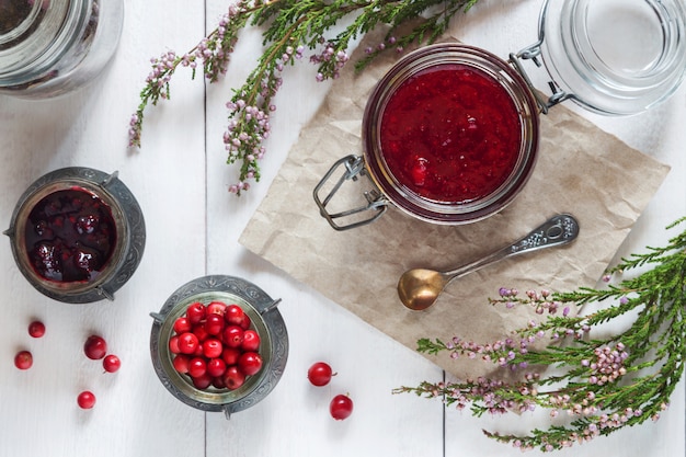 Glas Preiselbeermarmelade mit Beeren auf weißem Holztisch