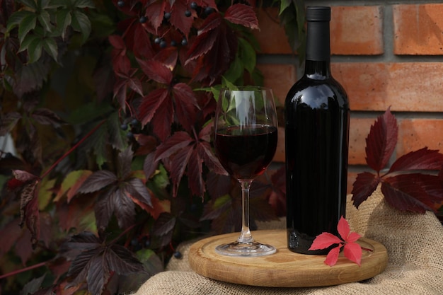 Glas Rotwein auf Holzhintergrund mit Herbstlaub und Flasche