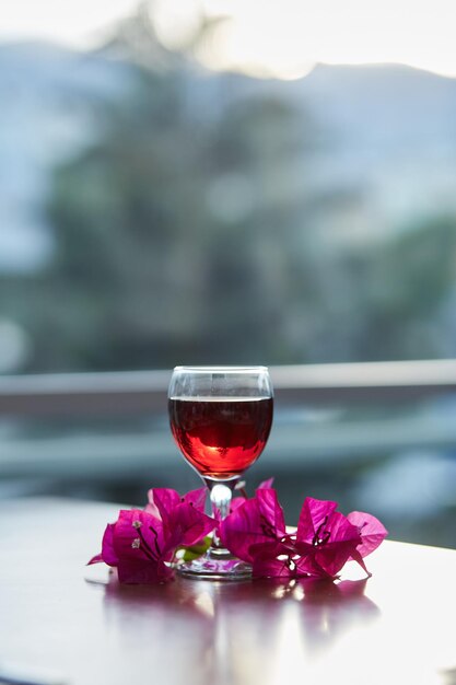 Glas Rotwein auf verschwommenem Berghintergrund Dekorationen aus rosafarbenen Bougainvillea-Blumen Blaue Stunde Fotografie Kopieren Sie Platz