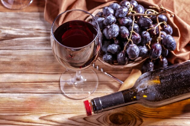 Glas Rotwein, Flasche und rote Trauben auf einem Holztisch.