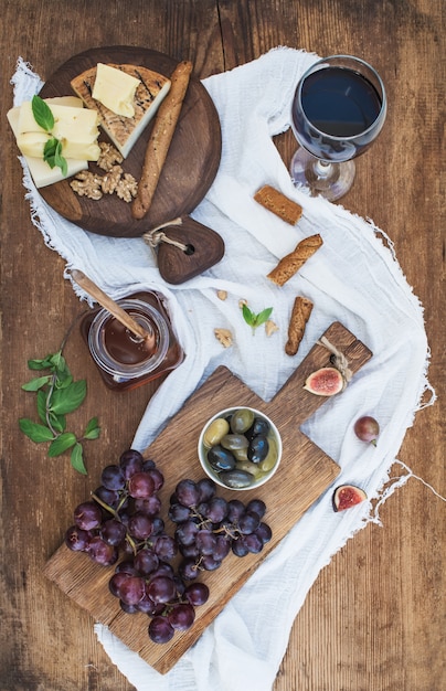 Glas Rotwein, Käsebrett, Trauben, Walnüsse, Oliven, Honig und Brotstöcke auf rustikalem Holztisch